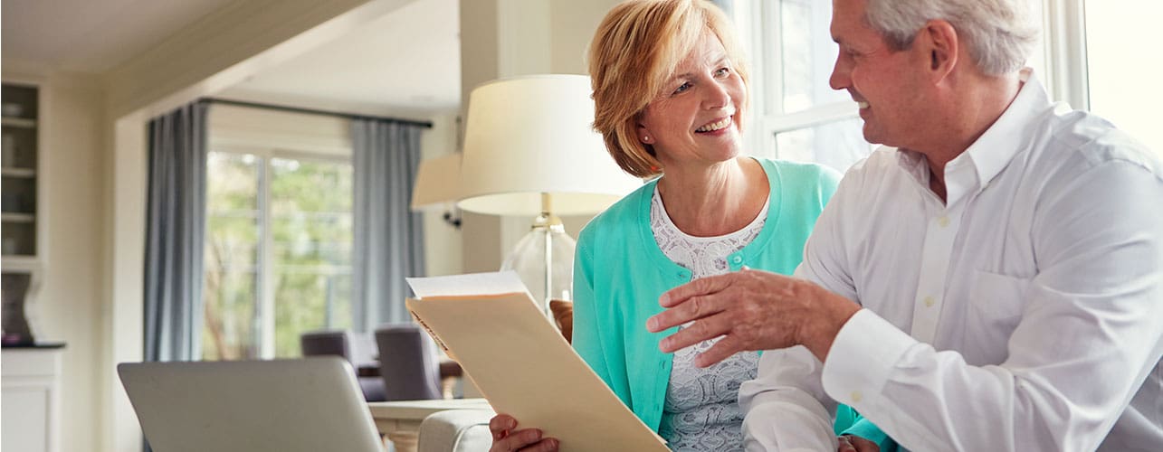 Senior couple talking about finances with a folder and laptop in hand.