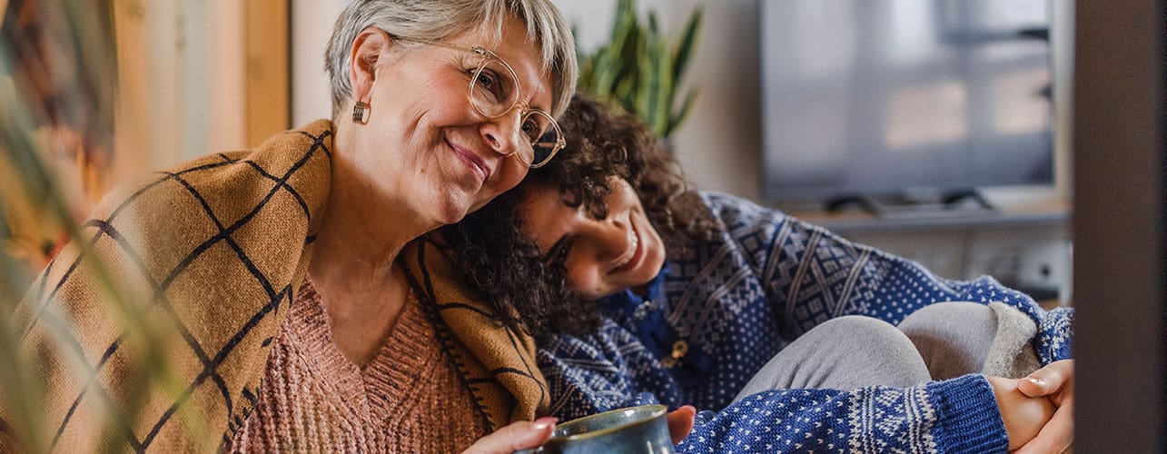 Grandmother and granddaughter resting together while they enough their hot coffee on a chilly winter morning.