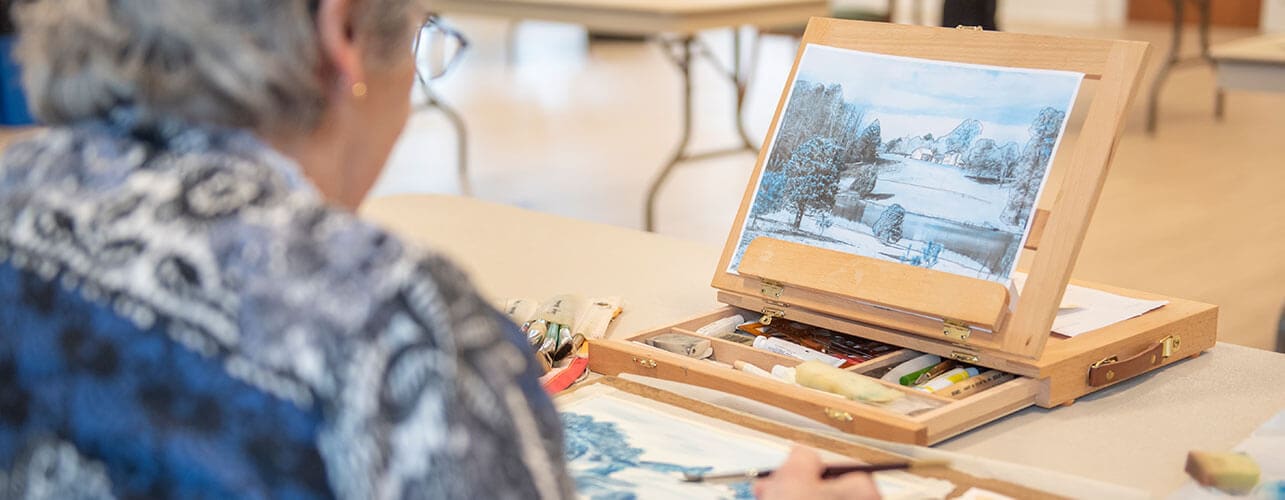 Senior woman painting a beautiful snowscape watercolor.